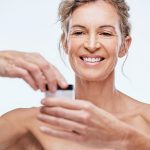 Shot of a mature woman holding up a beauty product against a while background